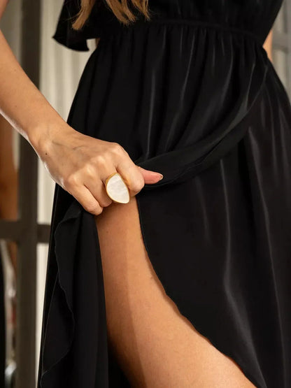 Close-up of a woman holding the flowing fabric of a black Soirée Midi Dress, showcasing its elegant slit and smooth silhouette.