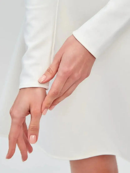 Elegant close-up of a woman's hand on the sleeve of the Ivory Sculpt Dress, showcasing its minimalist design.