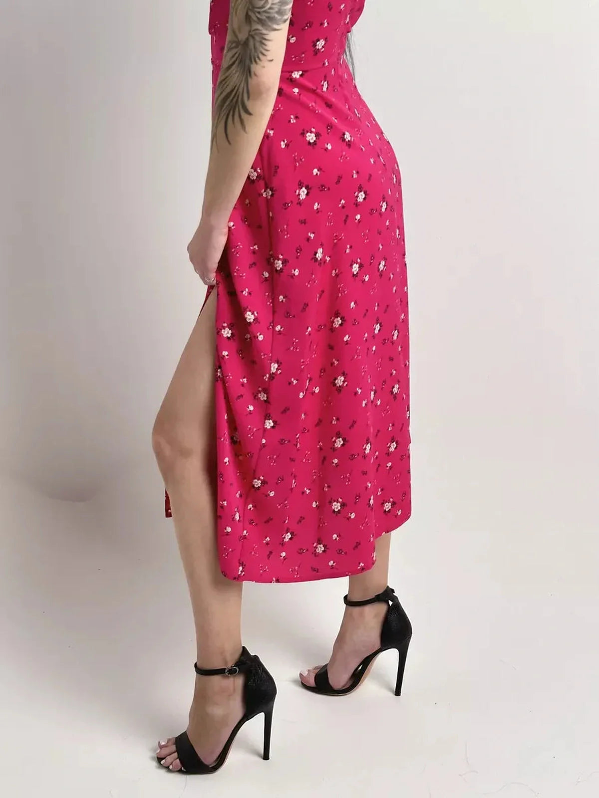 Side view of a model wearing a pink floral midi dress with a thigh-high slit and stiletto heels.