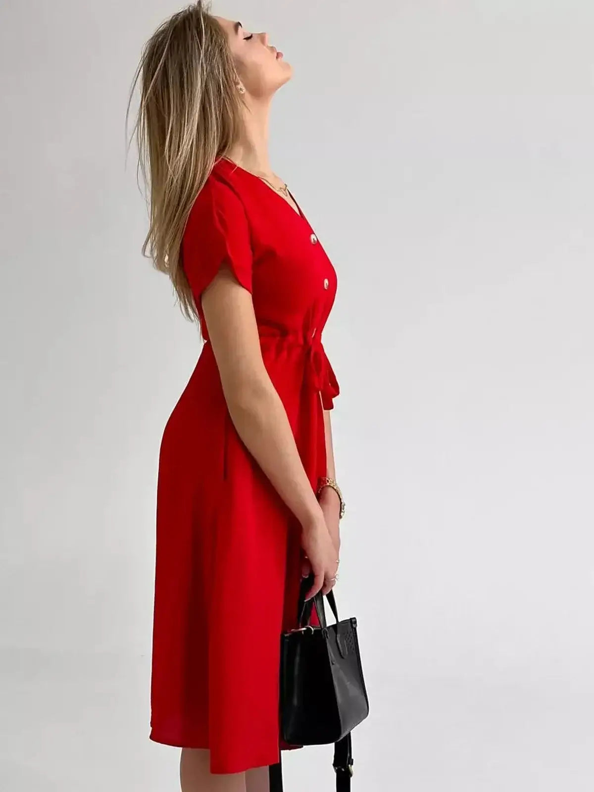 Woman wearing a crimson midi dress with a button-front and waist tie, styled with a black handbag.