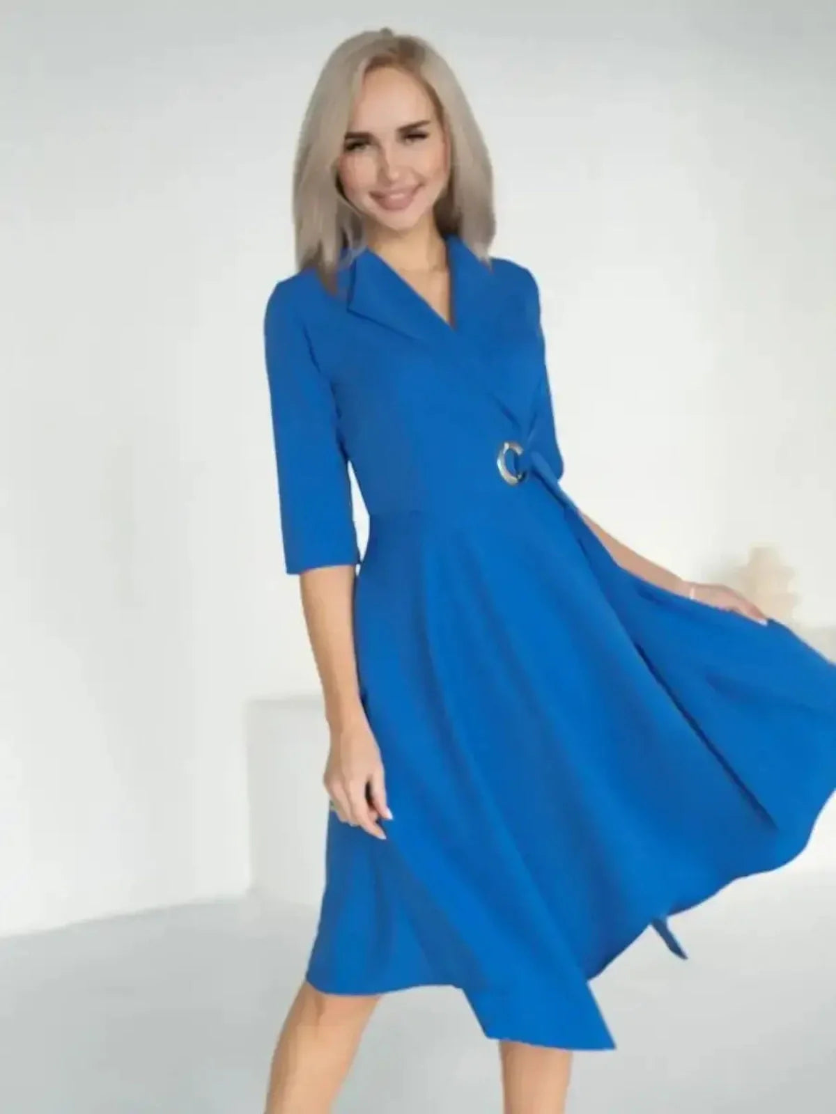 Woman in a striking sapphire blue midi dress with a wrap silhouette and metallic waist detail.