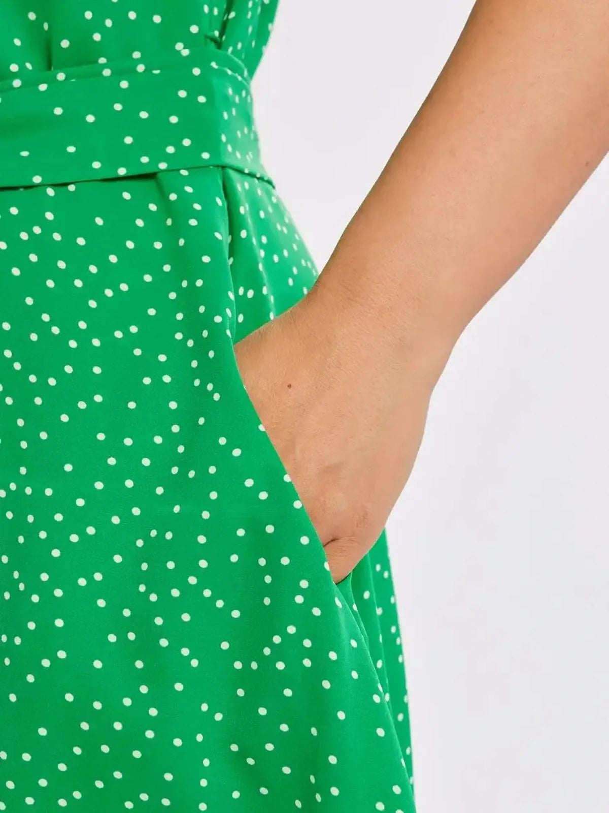Close-up of hand in pocket of vibrant green Garden Dot Midi Dress with white polka dots, showcasing its stylish design.