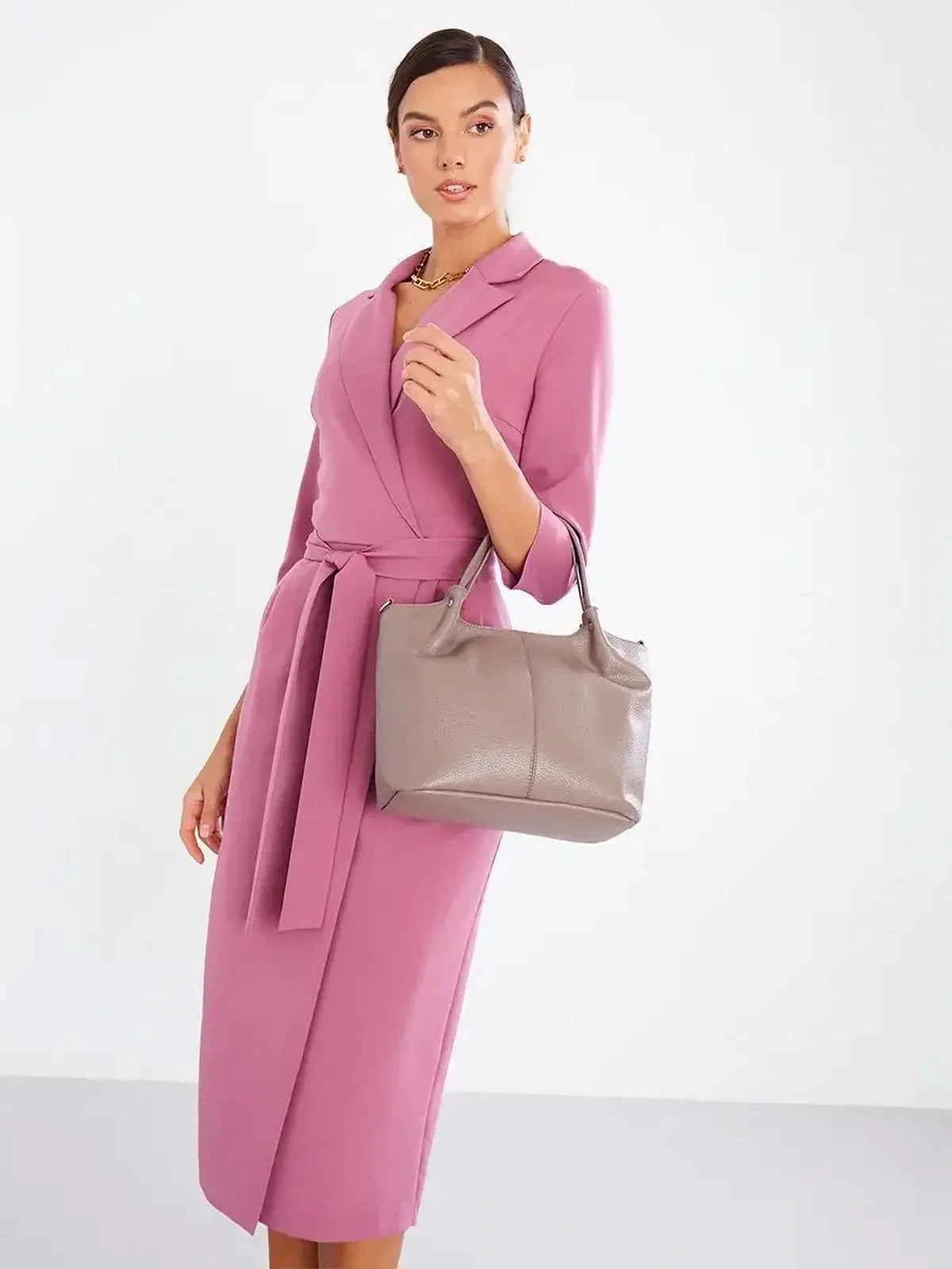 Stylish woman in a blush wrap midi dress with belted waist and three-quarter sleeves, holding a gray handbag.