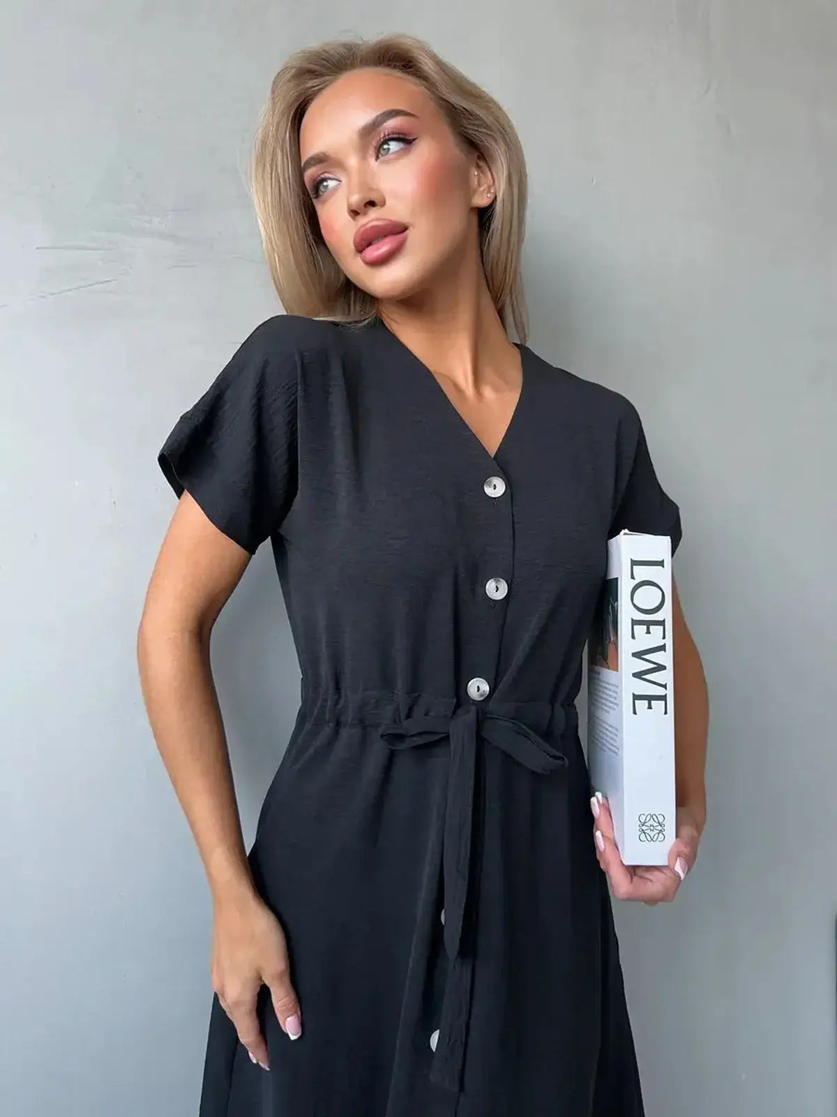 Model wearing the Iconic Ease Midi Dress, a black button-front dress featuring a tie waist and V-neckline.