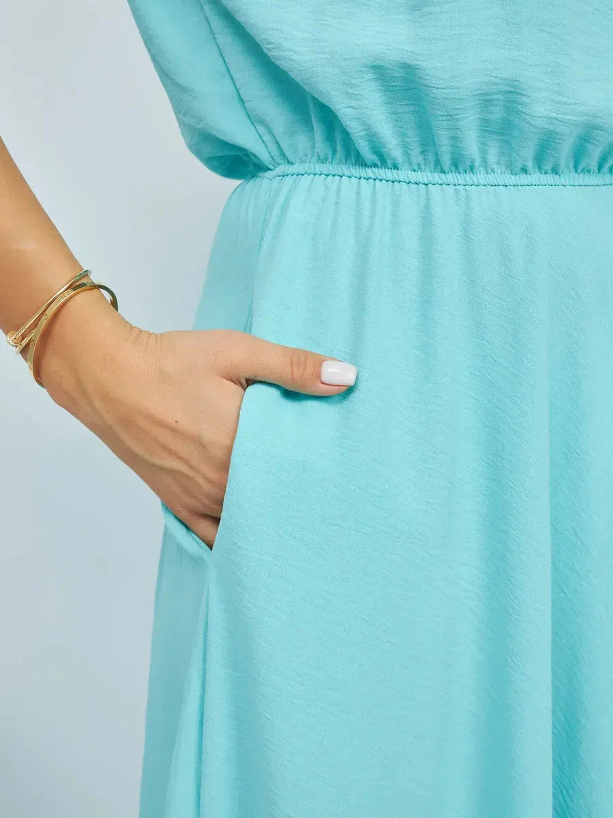 Close-up of a hand in the pocket of a light blue maxi dress, highlighting the elegant design and fabric.