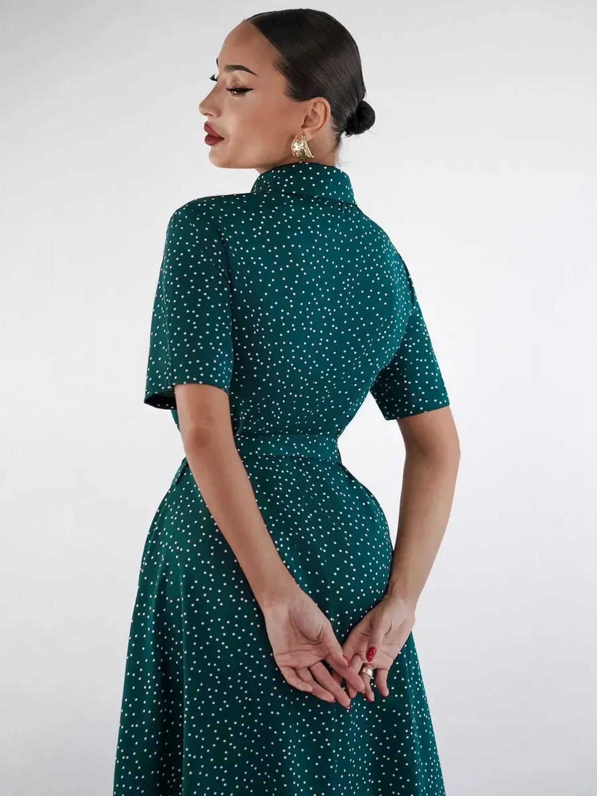 Back view of a woman in an emerald dot midi dress with a fitted silhouette and short sleeves.