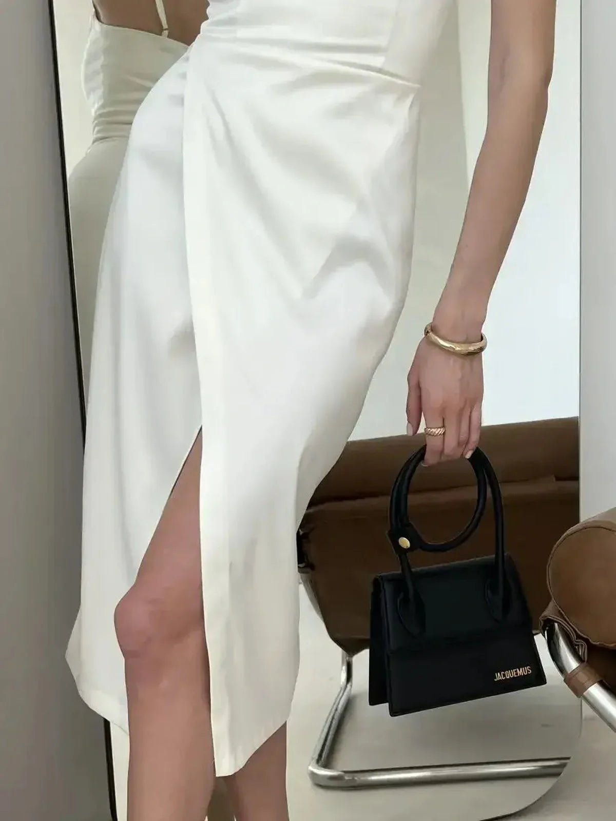Model showcasing the Opal Charm Midi Dress in ivory satin with a stylish front wrap slit and a chic black handbag.