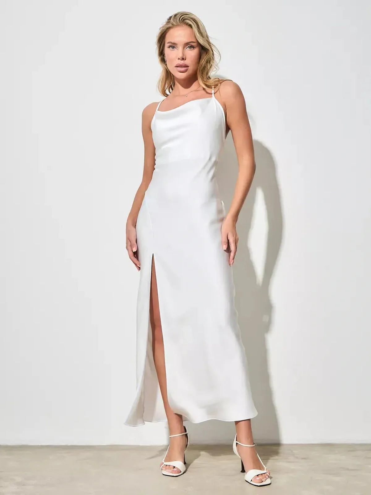 Model showcasing the Lustrous Charm Midi Dress, a sleek white satin dress with a thigh-high slit, perfect for summer weddings.
