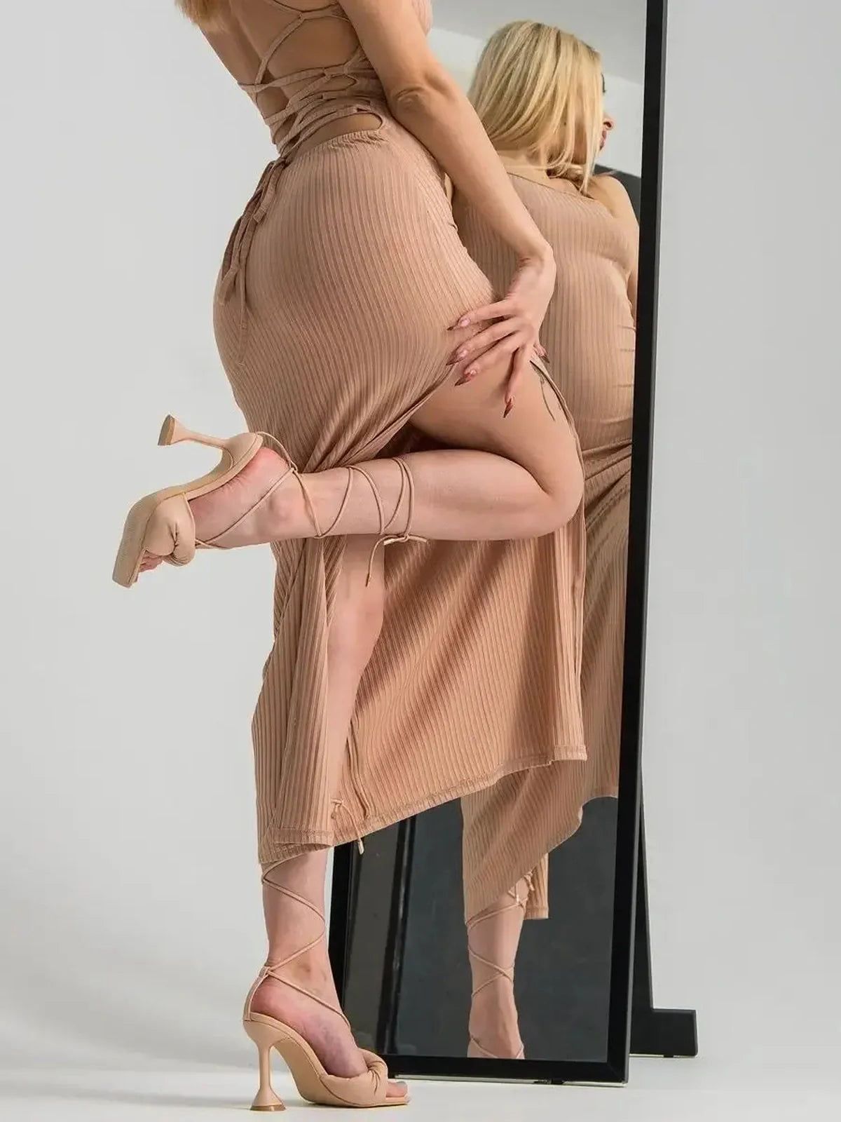 Model showcasing a nude lace midi dress with a corset back and strappy heels in front of a mirror.