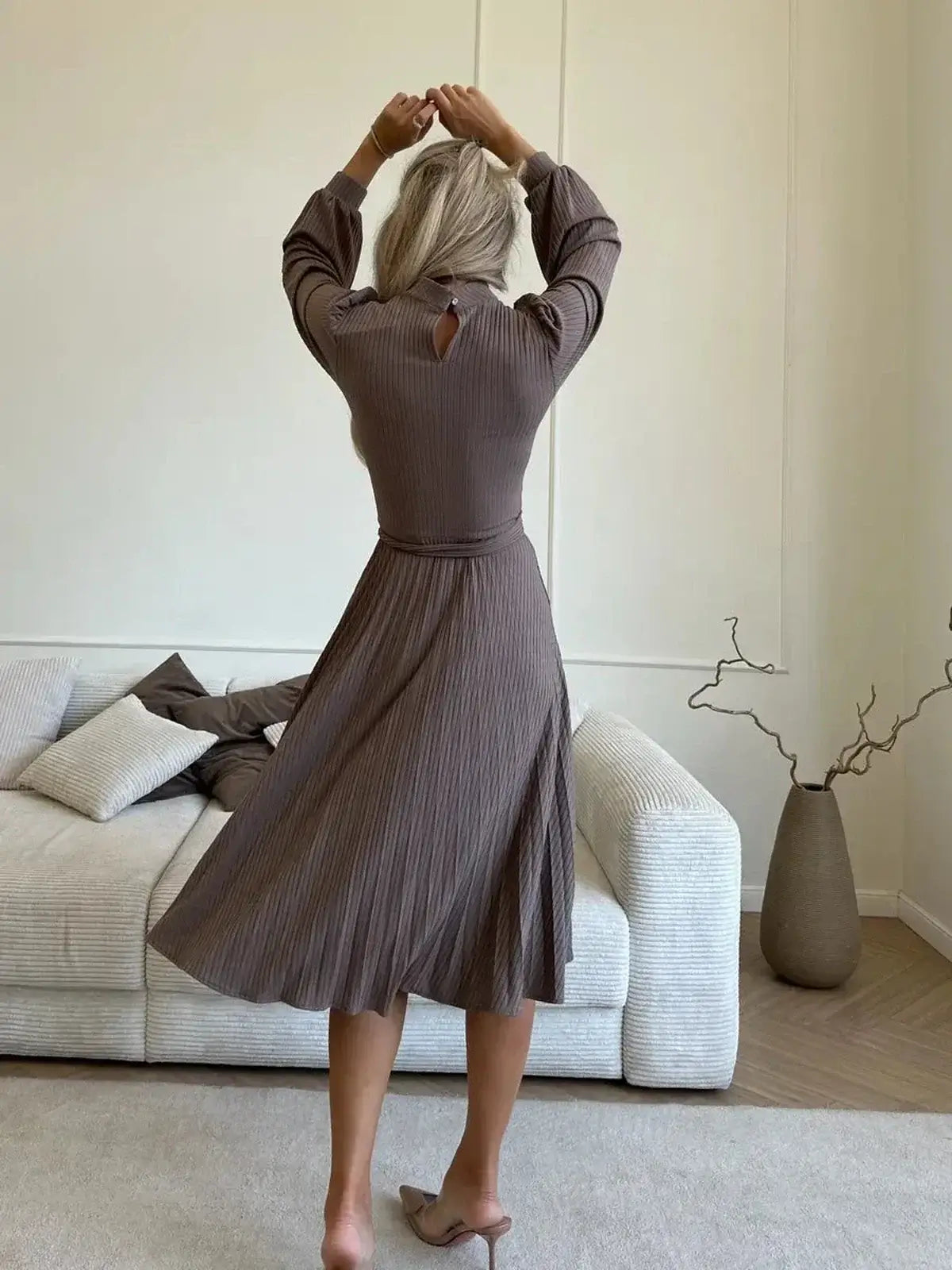 Back view of a woman in a Plissé Charm Midi Dress, showcasing its pleated skirt and elegant ribbed texture in coffee hue.