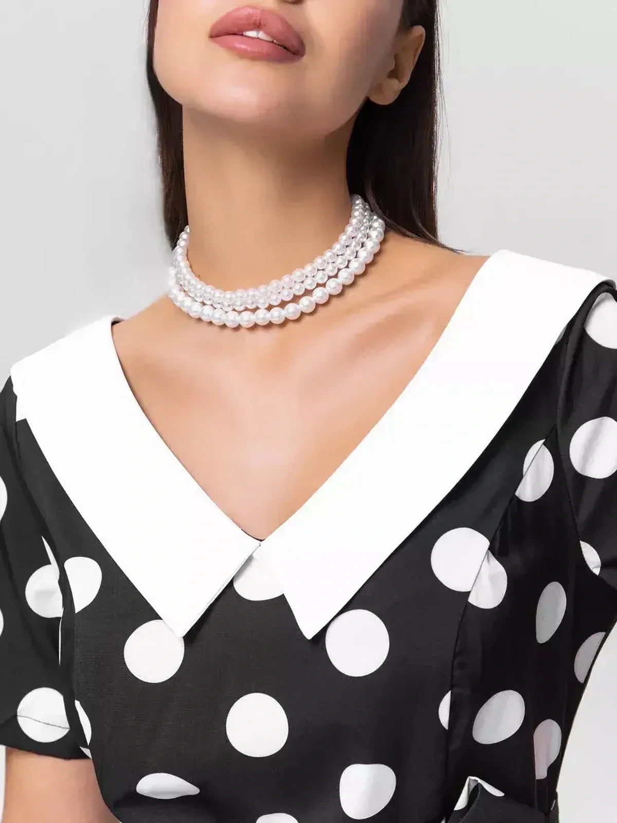 Close-up of the collar and neckline of the Midi Dress Luna Dot, featuring polka dots and a stylish pearl necklace.