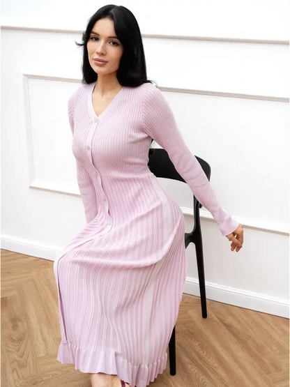 Model wearing a pink Crystal Knit Midi Dress with ribbed texture, seated on a chair, showcasing elegant fit and fluted hem.
