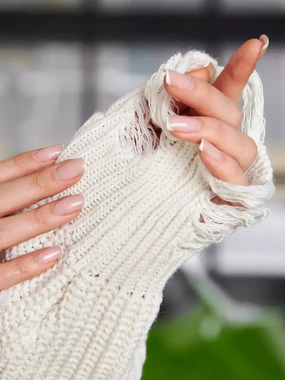 Close-up of a hand holding a soft ivory knit fabric with raw-cut edges, showcasing cozy texture and modern style.