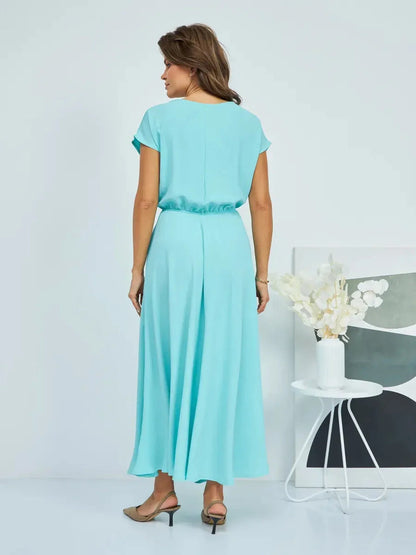 Back view of a woman in a light blue maxi dress, showcasing elegant draping and a flattering silhouette.