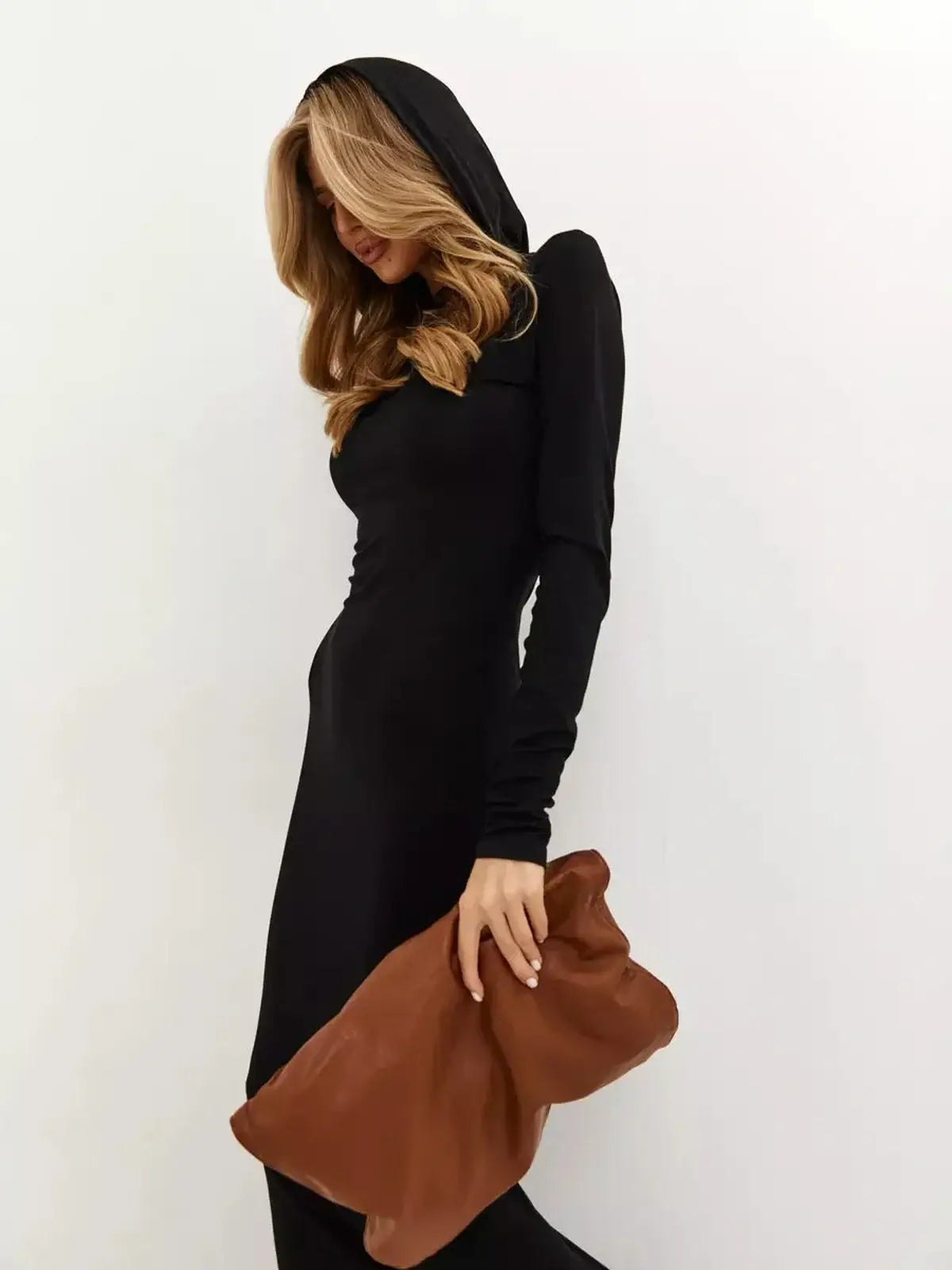 Woman wearing a Noir Maxi Dress with a hood, showcasing minimalist style and urban elegance, holding a brown clutch.