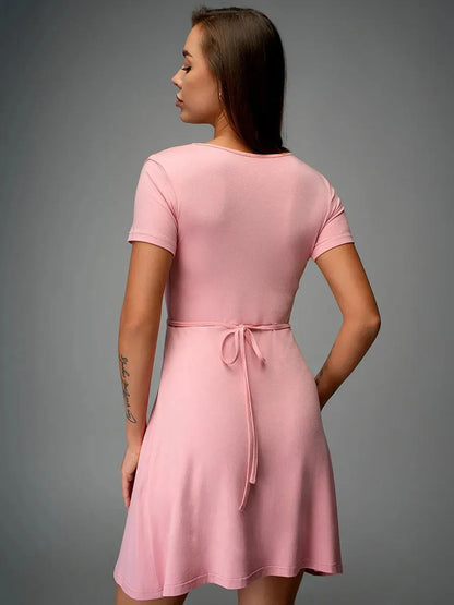 Back view of a blush pink wrap mini dress featuring a tie-back detail, showcasing a flattering and feminine style.