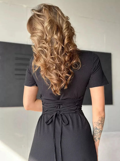 Back view of a woman in a black ribbed midi dress featuring a sculpted corset back and styled curls.