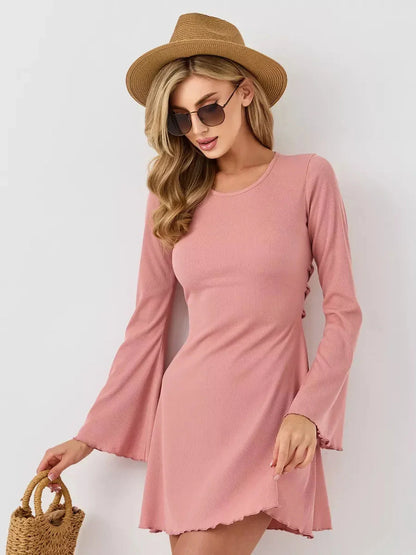 Model wearing a Blush Aura pink mini dress with flared sleeves, stylish sunglasses, and a straw hat.