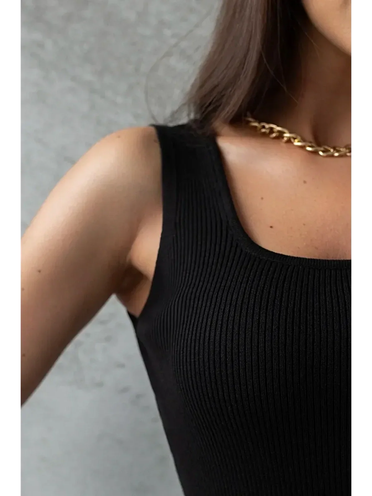 Close-up of a woman wearing a black ribbed mini dress, showcasing a sleek silhouette and a gold chain necklace.