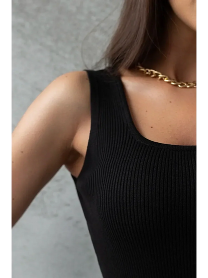 Close-up of a woman wearing a black ribbed mini dress, showcasing a sleek silhouette and a gold chain necklace.