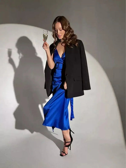 Elegant woman in a cobalt blue midi dress with black blazer, holding a champagne glass, showcasing modern glamour.