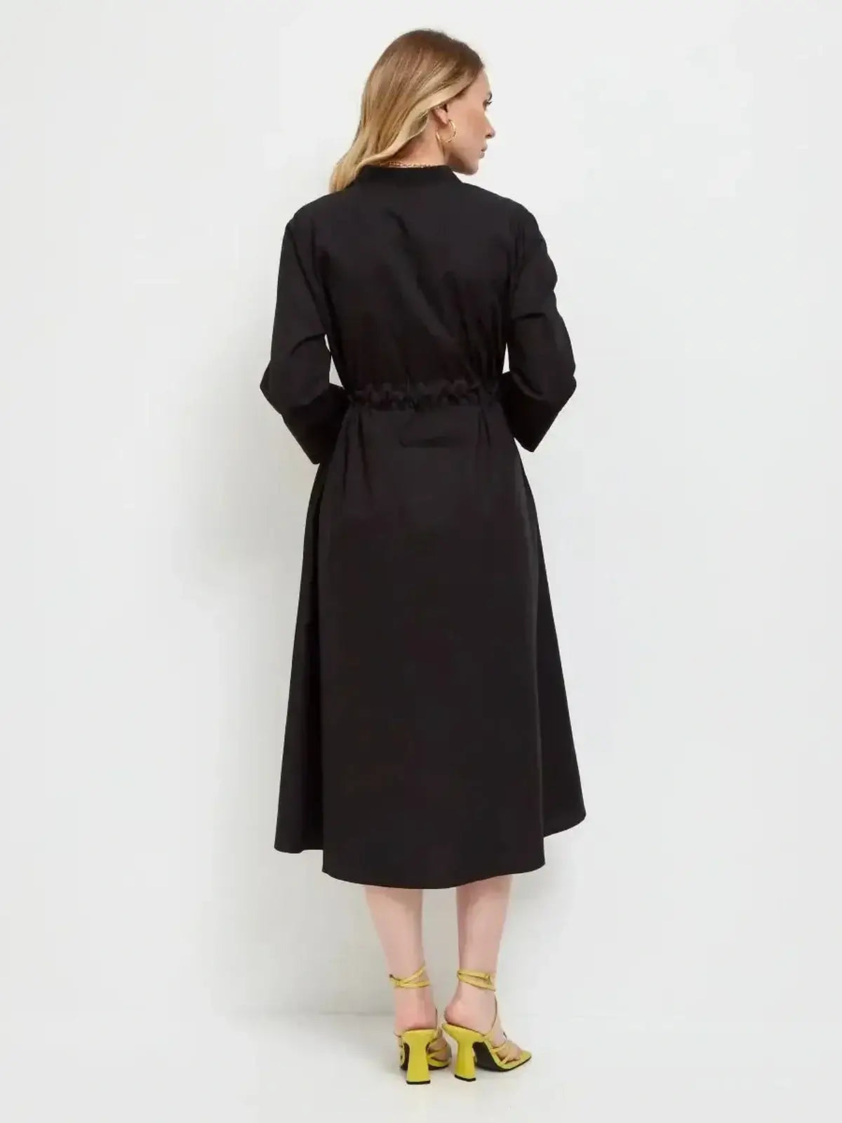 Back view of the Noir Grace Midi Dress in black, featuring a cinched waist and elegant A-line silhouette, paired with yellow heels.