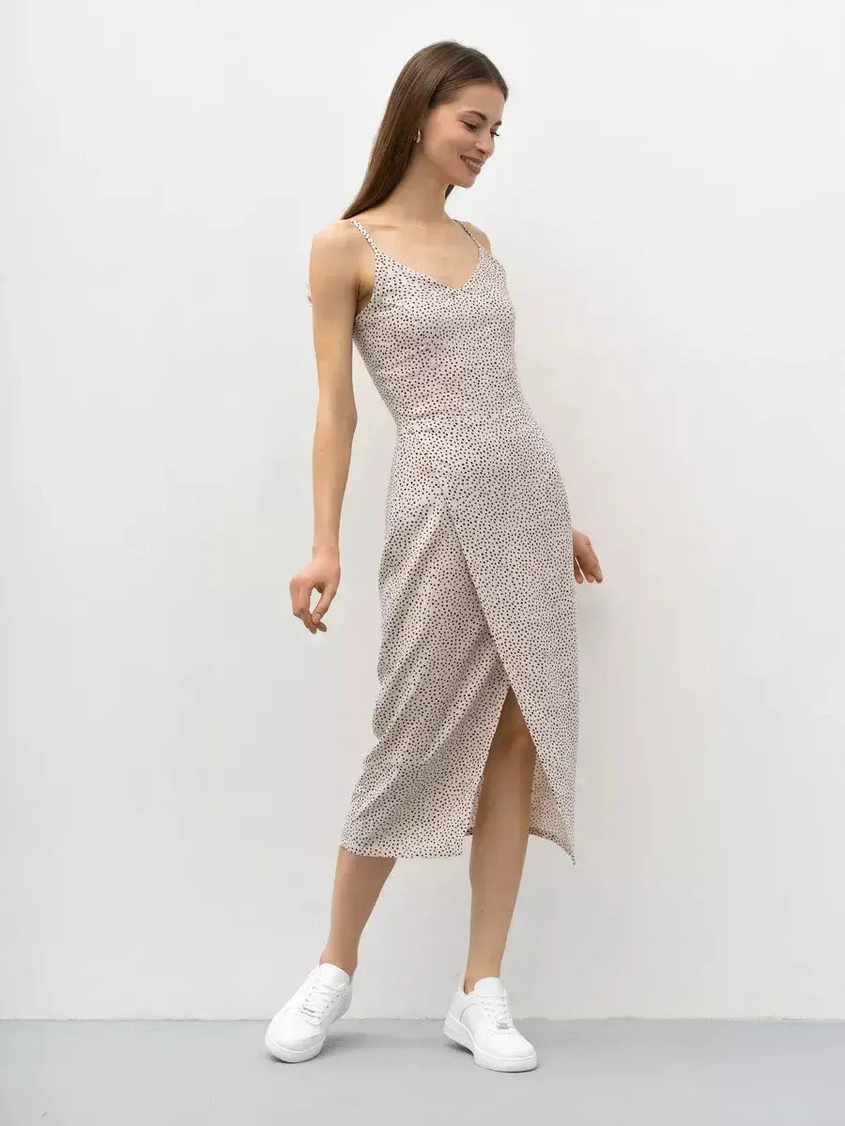 Model wearing a Dot Whisper Midi Dress with polka dots, showcasing a V-neckline and wrap-effect skirt, paired with white sneakers.