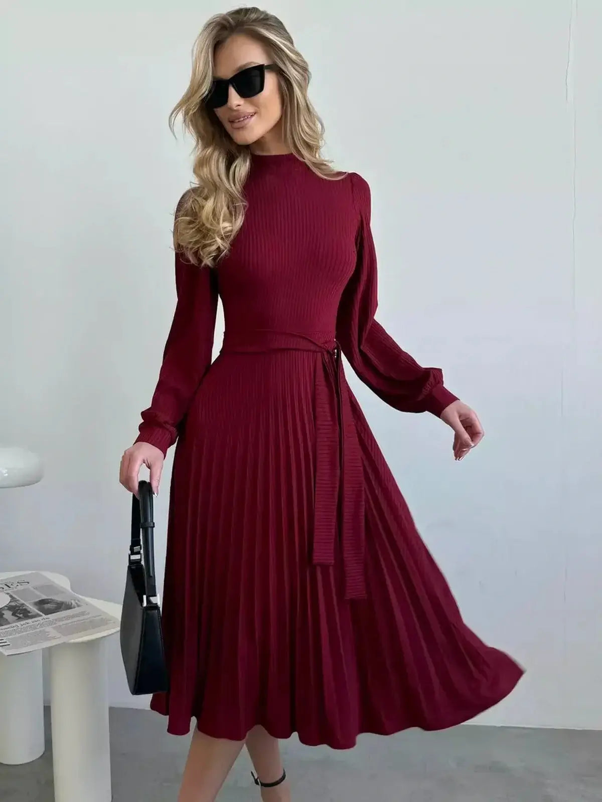 Elegant woman in a crimson midi dress with pleats, sunglasses, and a stylish bag, perfect for formal occasions.