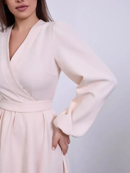 Close-up of a woman wearing a champagne-toned mini dress with a V-neck wrap and long puff sleeves.