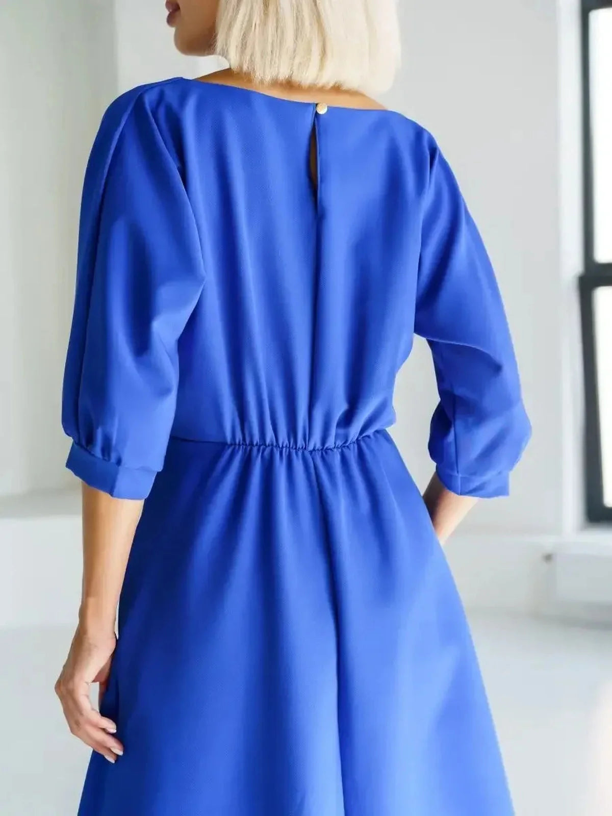 Back view of a model wearing a sleek sapphire belted midi dress, showcasing elegant structure and vibrant color.