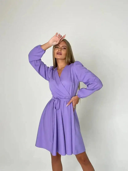 Model showcasing a lilac mini dress with long sleeves and a cinched waist, perfect for summer or wedding guest occasions.