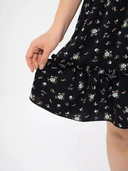 Close-up of hand holding tiered ruffle of a black floral dress, perfect for summer and special occasions.