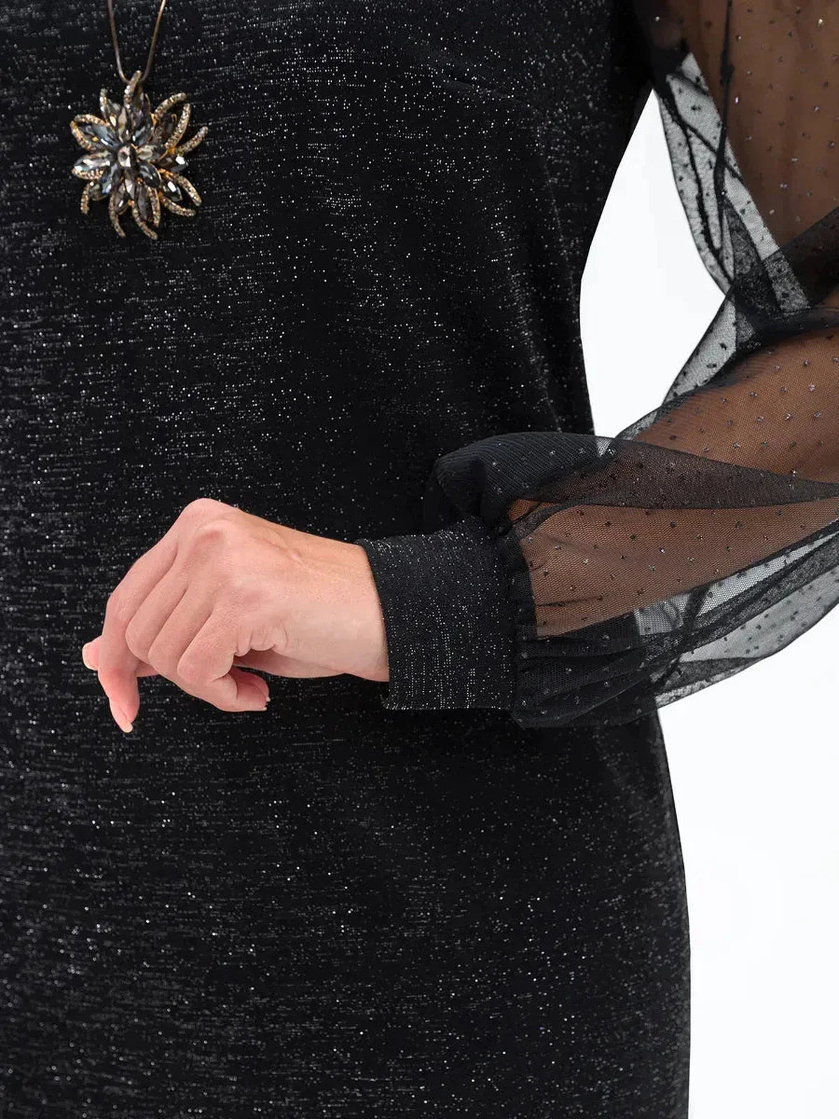 Close-up of elegant black midi dress with sheer mesh sleeves and shimmering detail, styled with a statement necklace.
