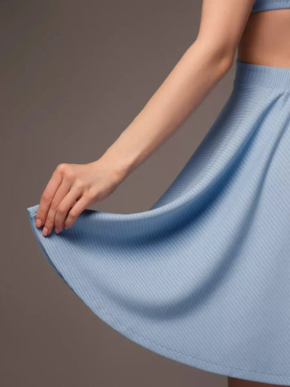 Close-up of a woman's hand holding the flared hem of a pastel blue mini skirt, showcasing its soft fabric and flow.