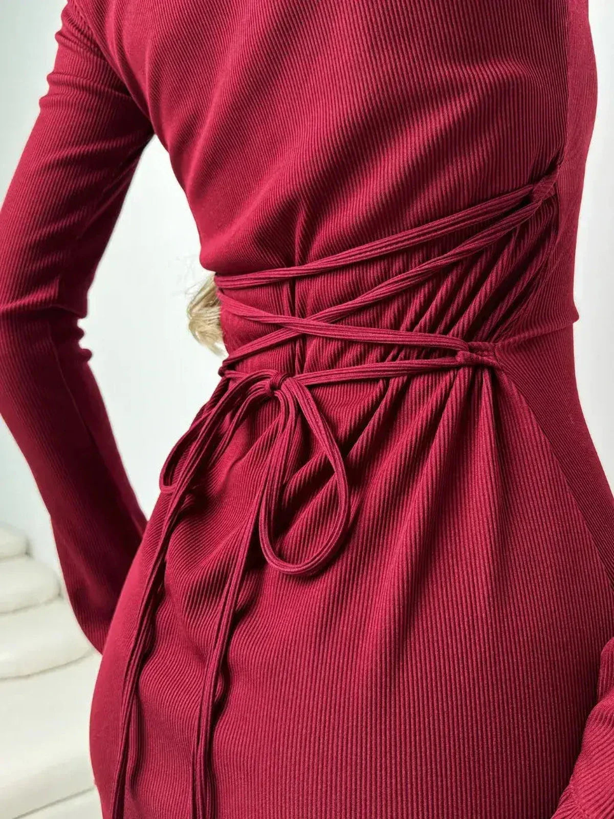Detail view of a fitted ribbed knit crimson dress showcasing romantic ruffles and a stylish tie design.