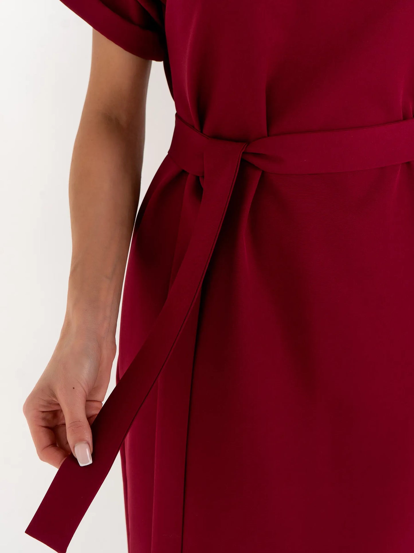 Close-up of a woman's hand holding the belt of a crimson mini dress, showcasing its elegant design and tailored silhouette.
