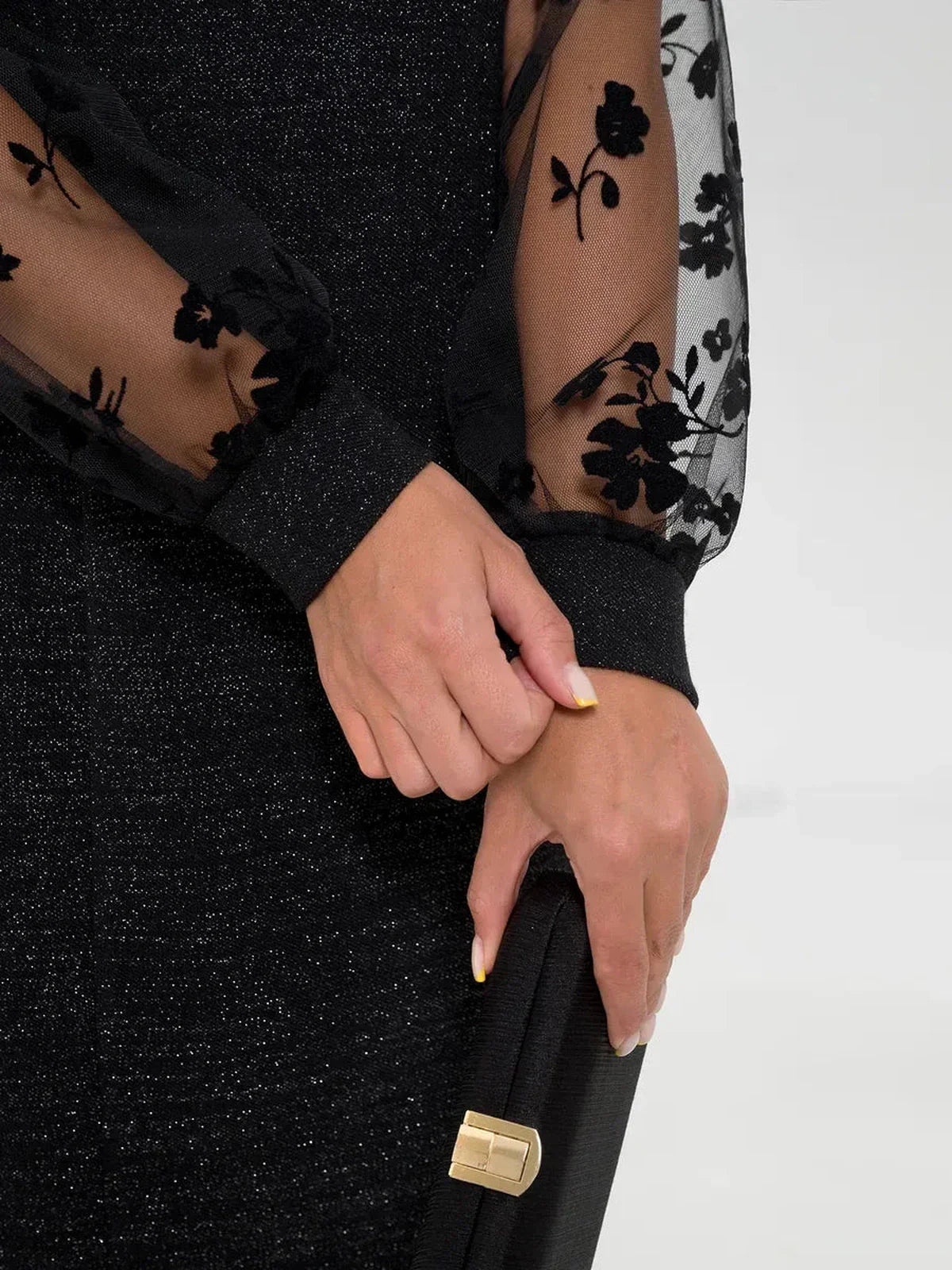 Close-up of hands wearing the Luxe Spark Midi Dress showcasing sheer floral sleeves and shimmering lurex fabric.