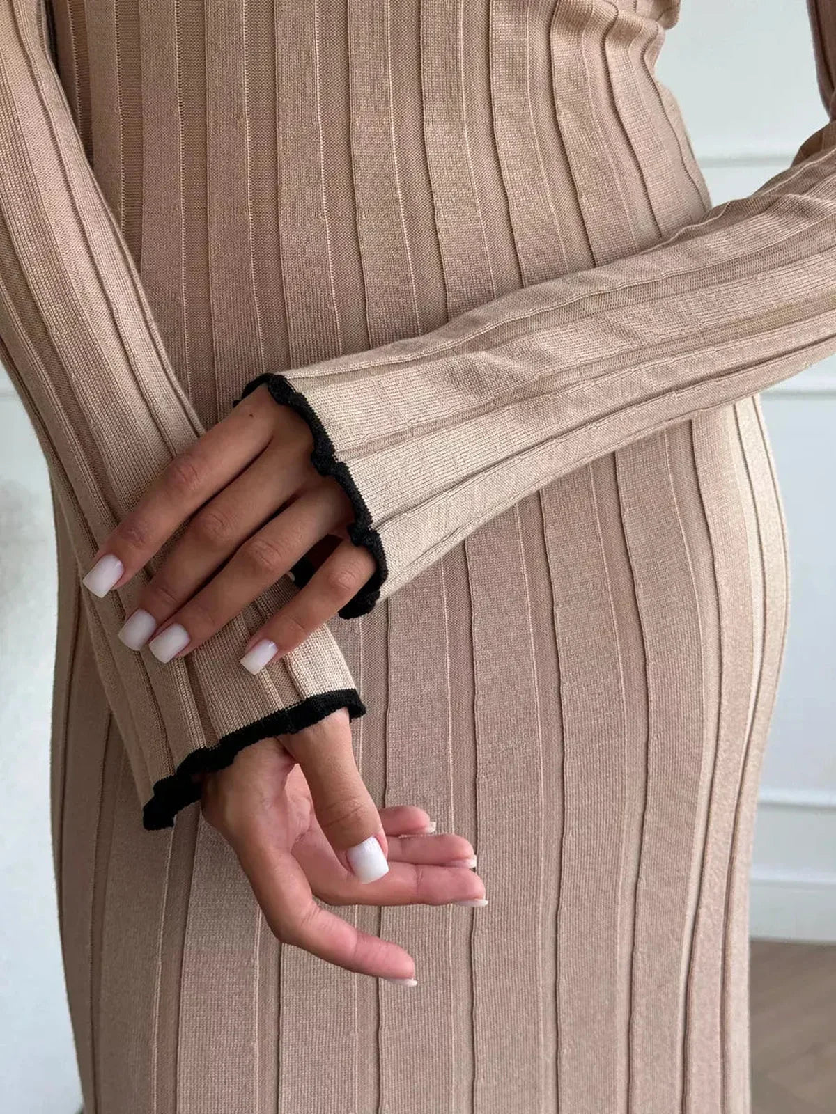 Close-up of hands wearing a soft ribbed beige dress with black trim, highlighting elegant fashion details.