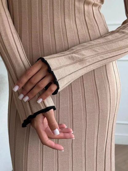 Close-up of hands wearing a soft ribbed beige dress with black trim, highlighting elegant fashion details.