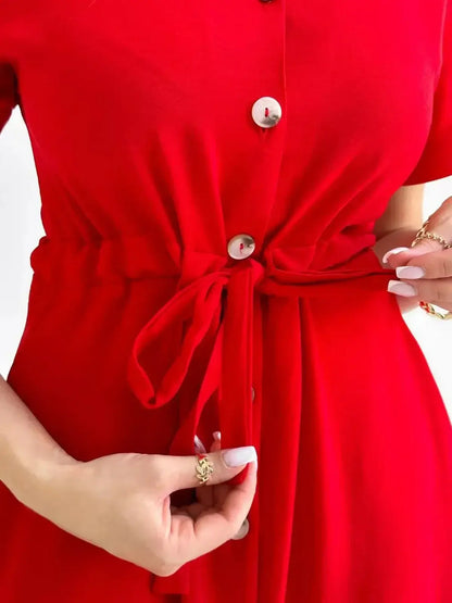 Close-up of a woman adjusting the tie on the waist of a vibrant red midi dress with buttons.
