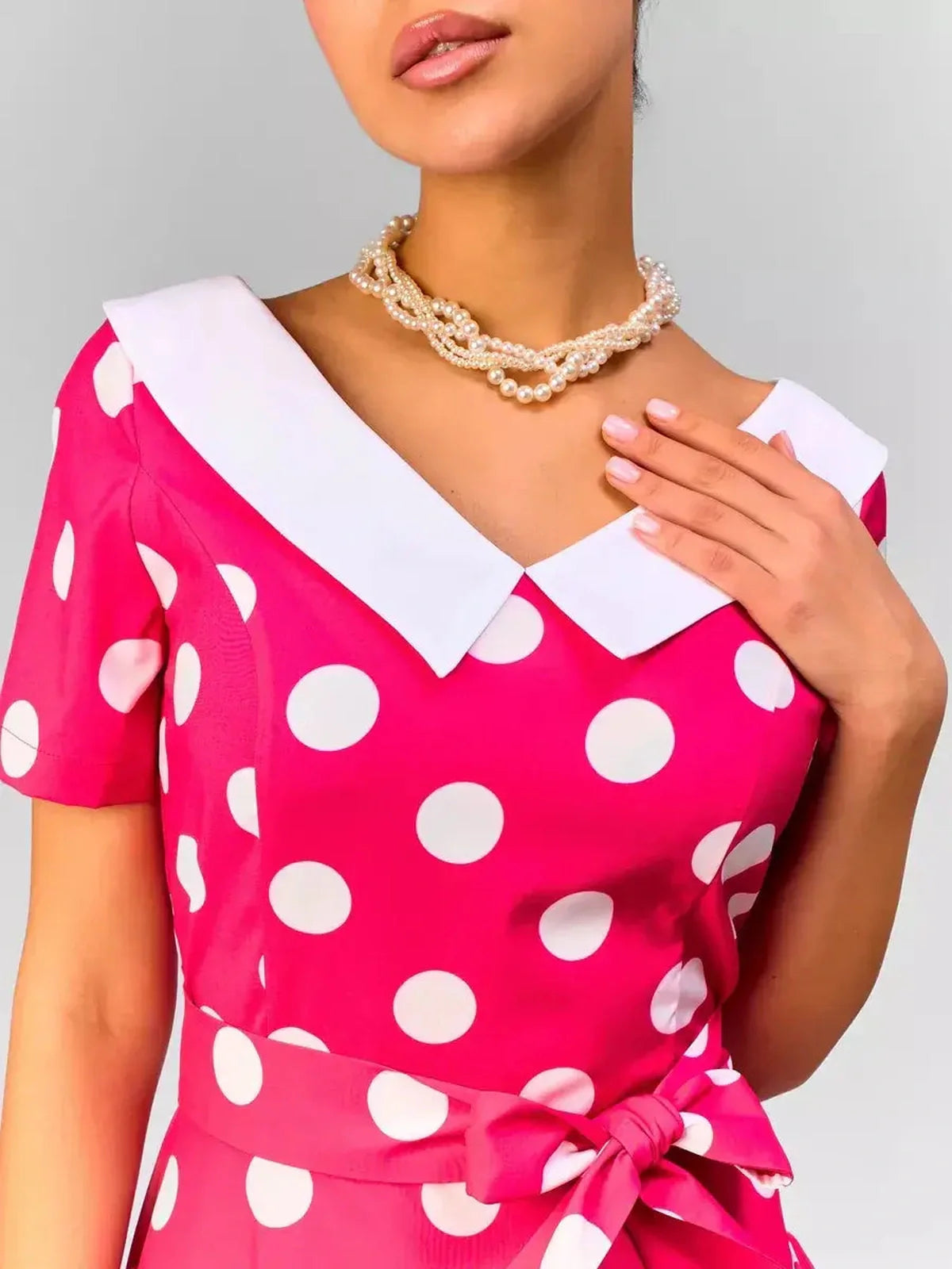 Close-up of a woman in a pink polka dot midi dress with a white collar, showcasing retro elegance and modern style.