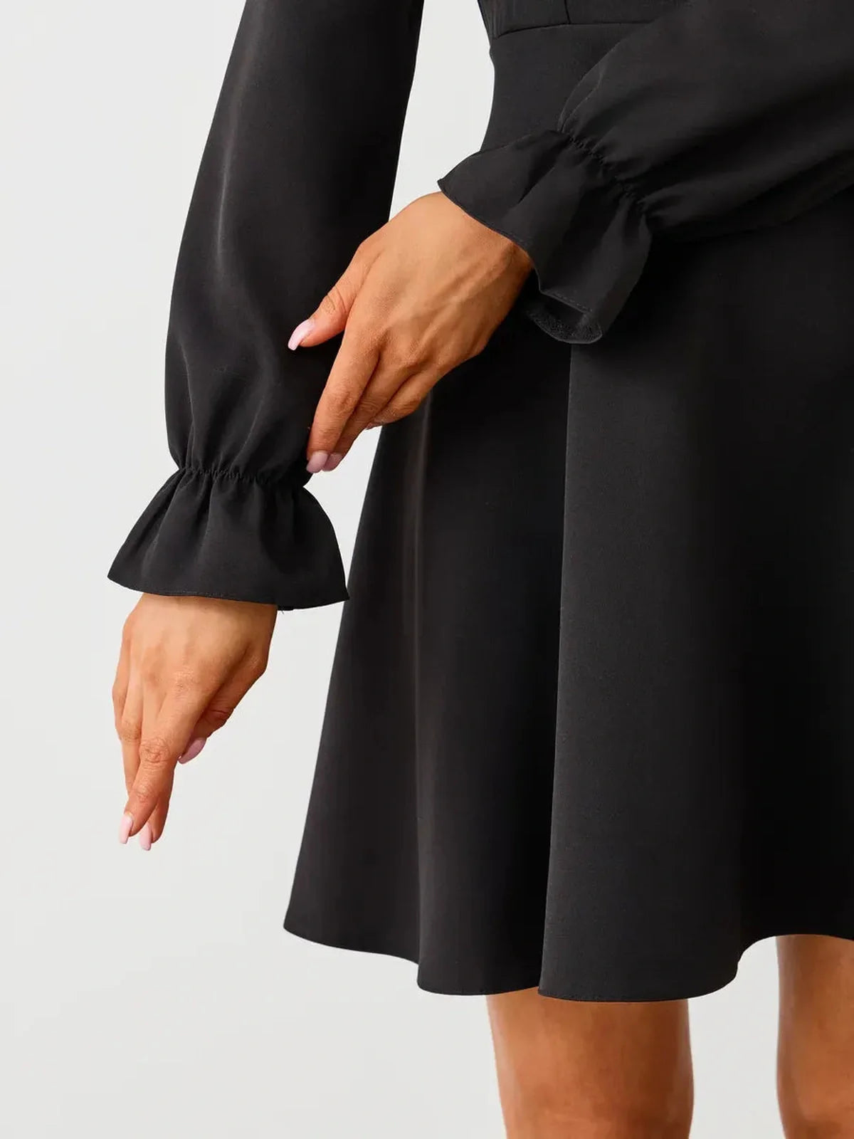 Close-up of a woman’s hands modeling the elegant sleeves of a black mini dress, showcasing a ruffled design.