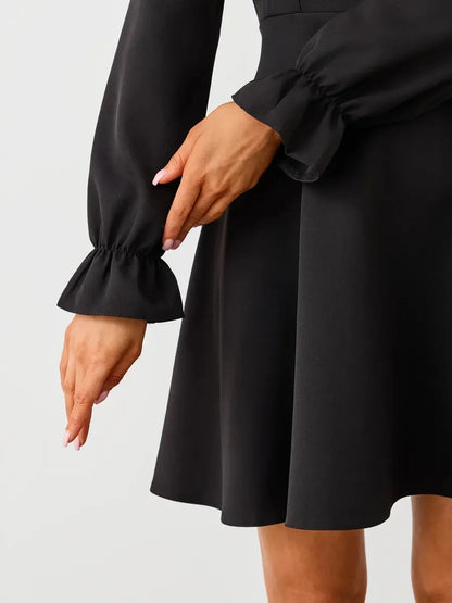 Close-up of a woman’s hands modeling the elegant sleeves of a black mini dress, showcasing a ruffled design.