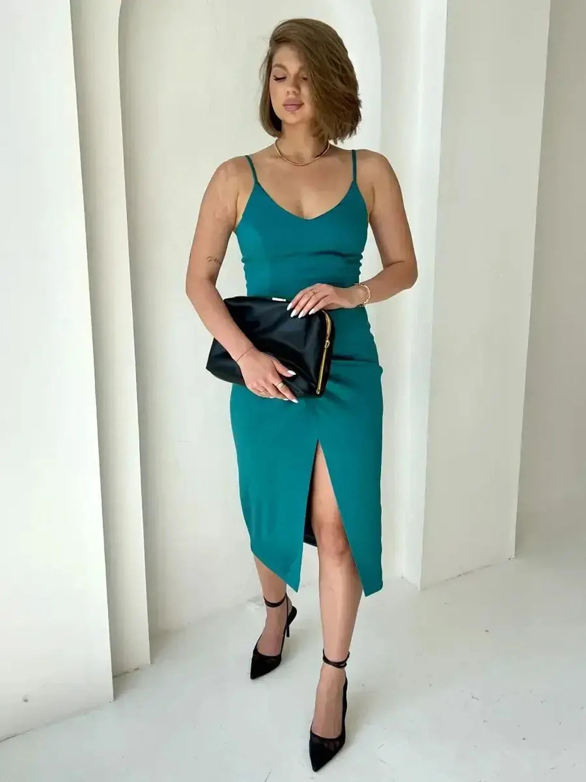 Elegant woman in a teal satin midi dress with thigh-high slit and black clutch, perfect for formal events.