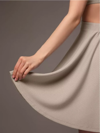 Woman's hand holding the hem of a light grey ribbed mini dress, showcasing its soft texture and playful flared design.