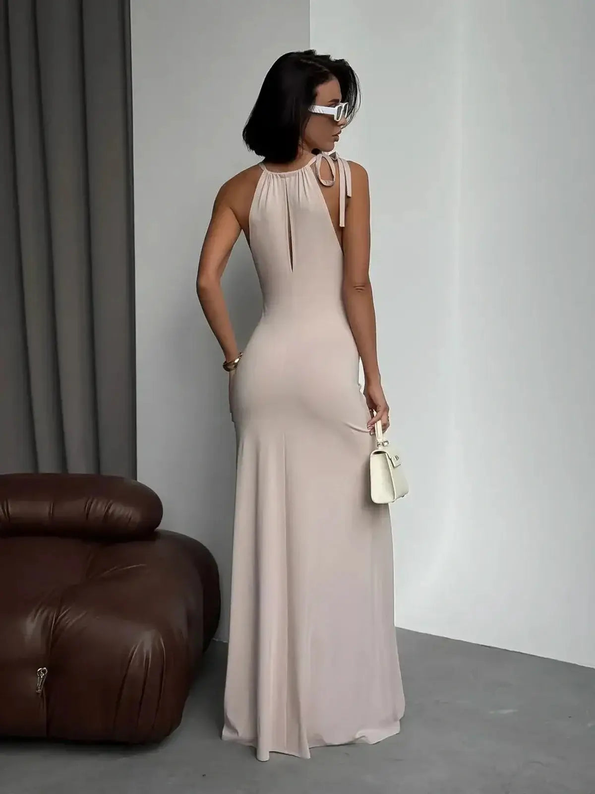 Elegant woman in a beige Serene Curve maxi dress with adjustable halter neck, showcasing a sculpted fit and sleek silhouette.