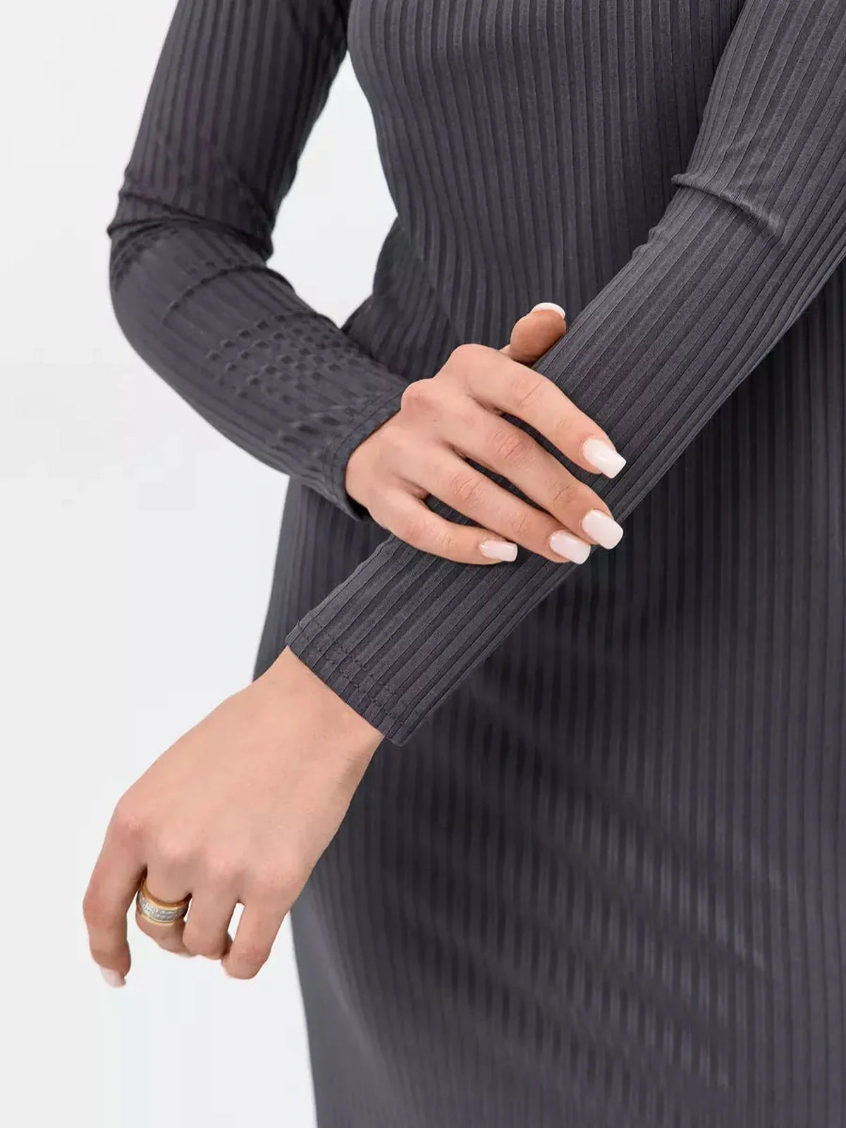 Close-up of women's hands adjusting the cuff on a grey ribbed midi dress, showcasing elegant fashion styling.