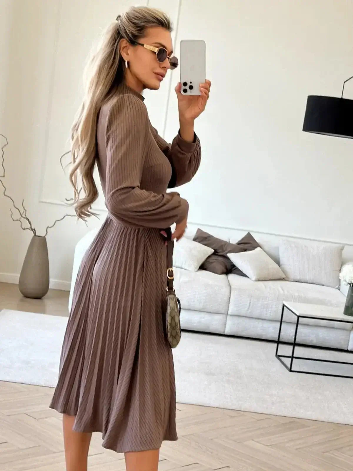 Model wearing a Plissé Charm Midi Dress in coffee color, showcasing a pleated skirt and elegant fit in a stylish indoor setting.