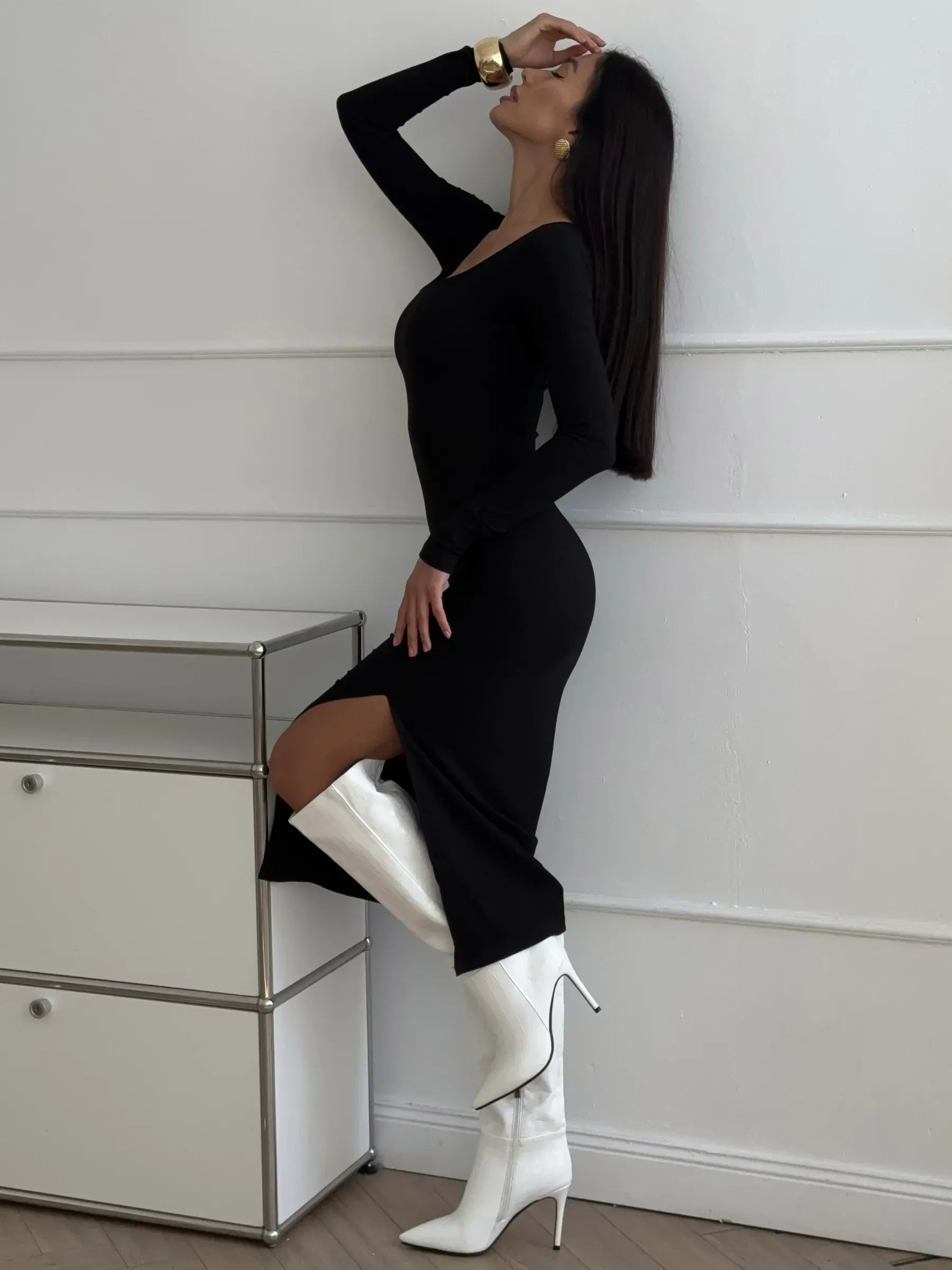 Stylish woman in a black midi dress with a thigh-high slit and white thigh-high boots, accentuating modern elegance.