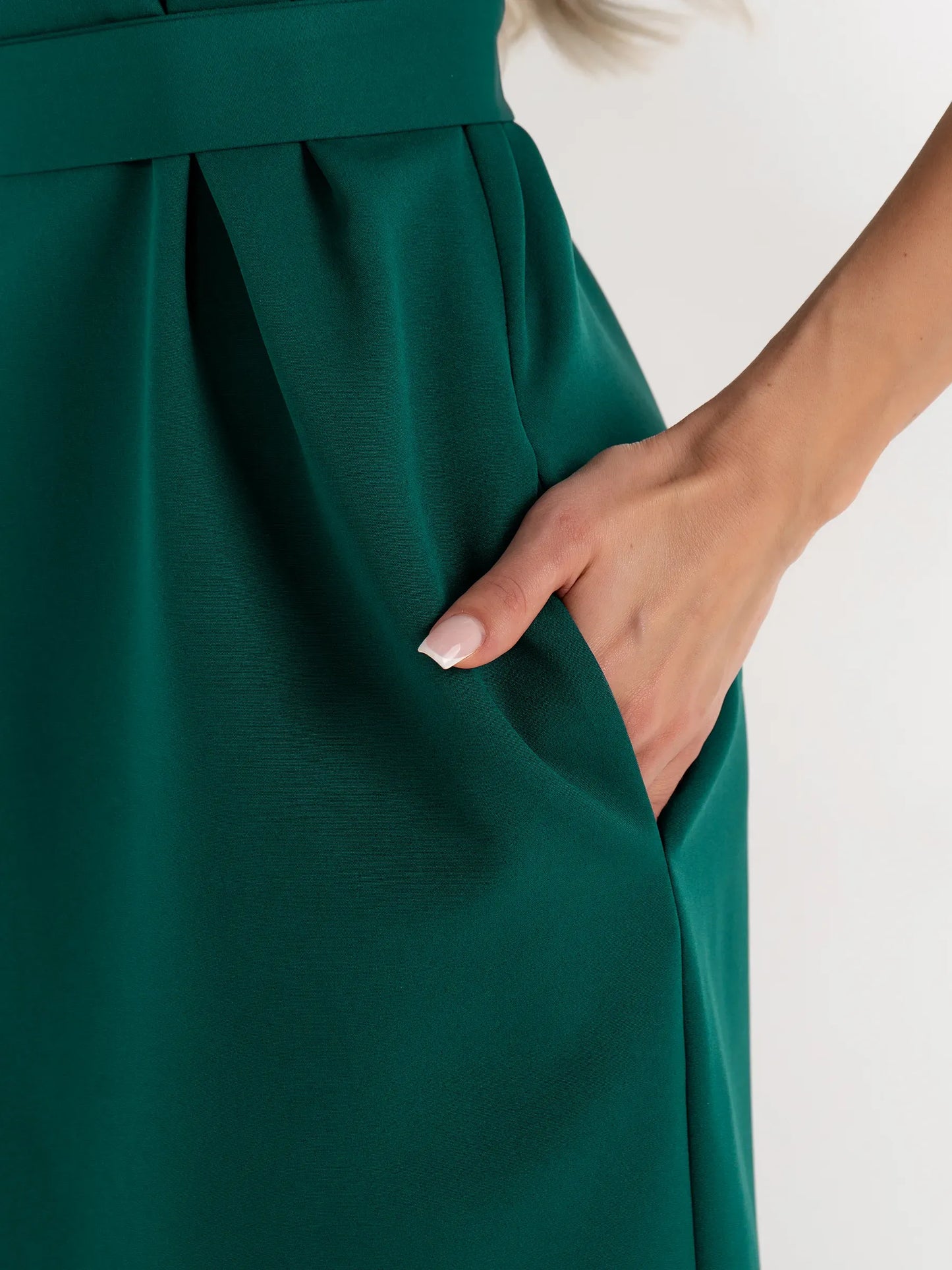 Close-up of a hand in the pocket of a tailored emerald green mini dress, highlighting its modern design.